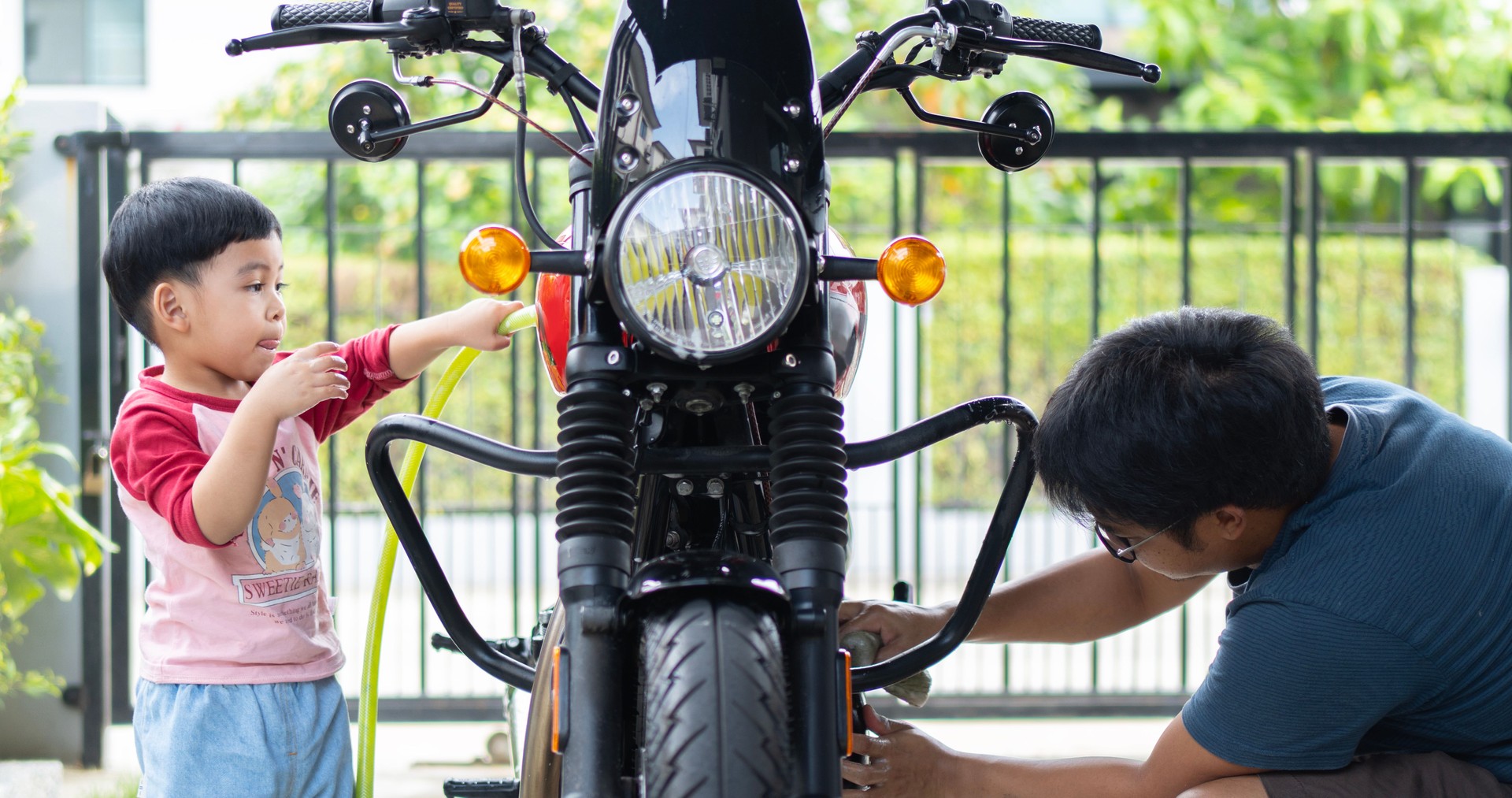 The happy boy and the father washing a motorcycle outdoor on the sunny day.